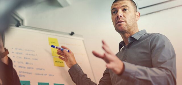 male presenter speaking to group in front of whiteboard