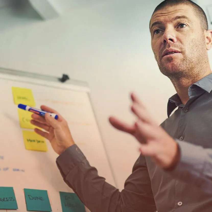male presenter speaking to group in front of whiteboard