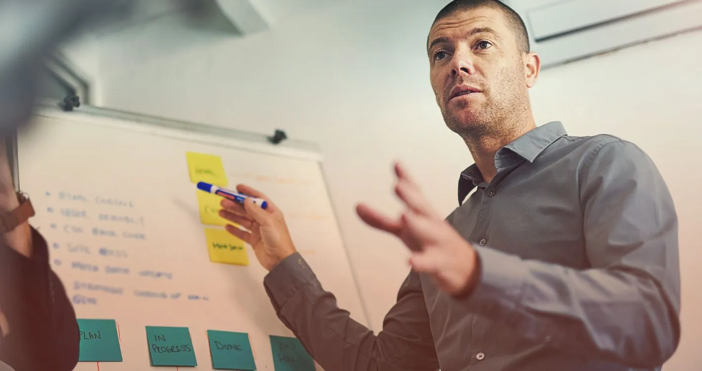 male presenter speaking to group in front of whiteboard