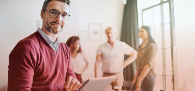 satisfied man with tablet in office with colleagues