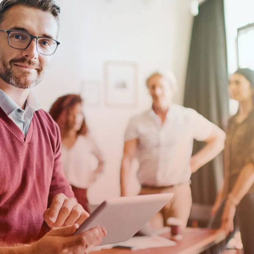 satisfied man with tablet in office with colleagues