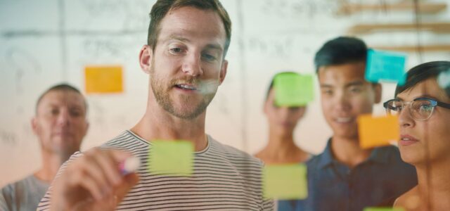 man writing on post-it note in group setting