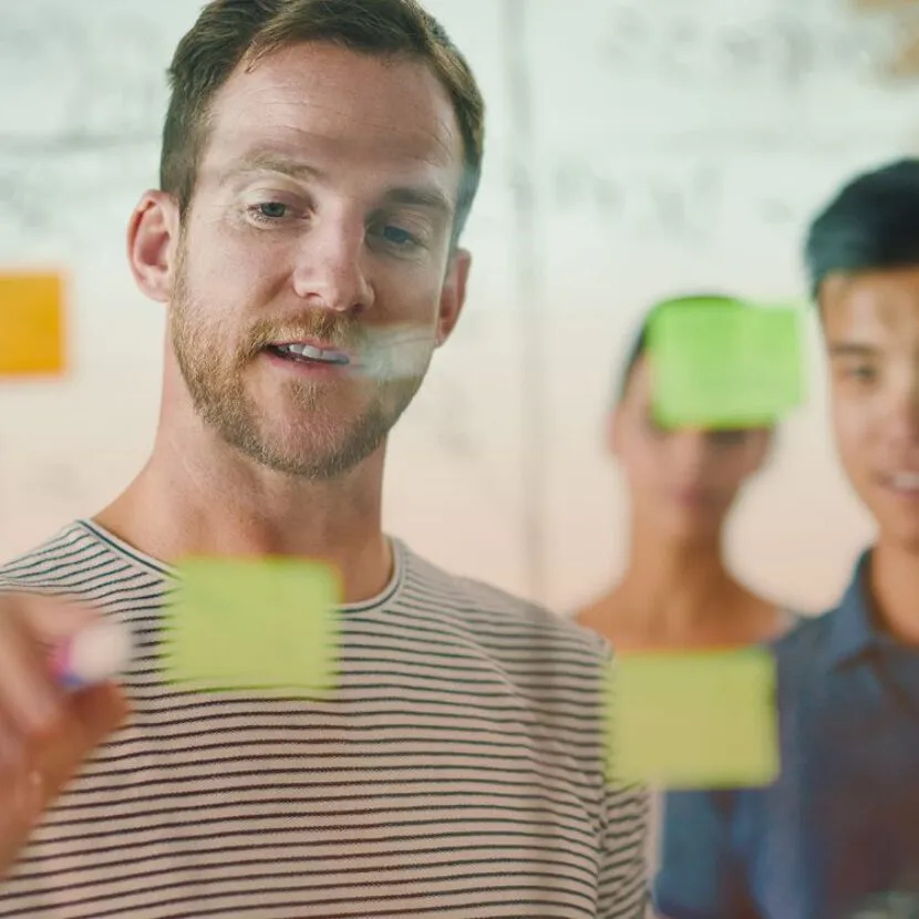 man writing on post-it note in group setting