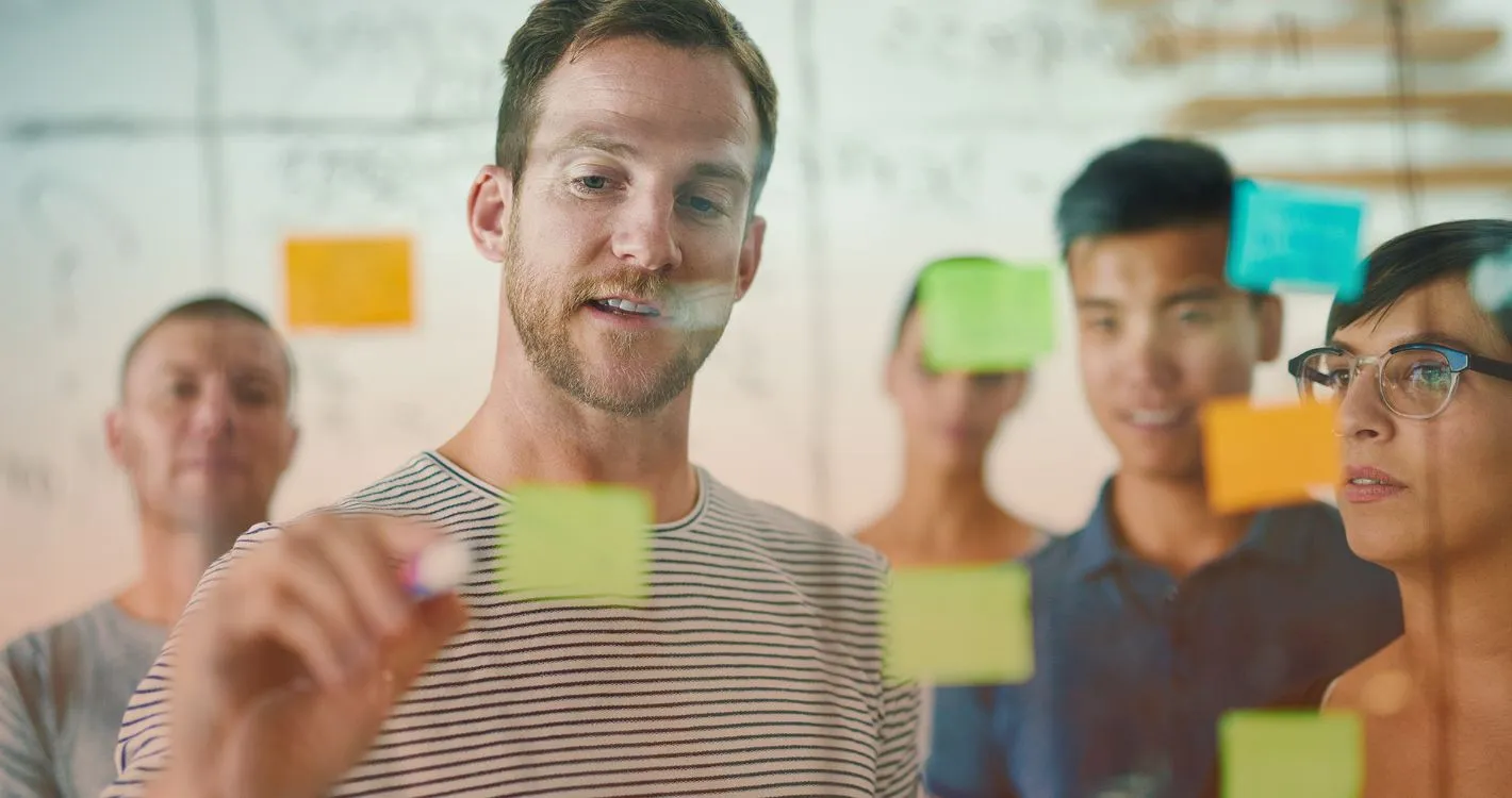 man writing on post-it note in group setting